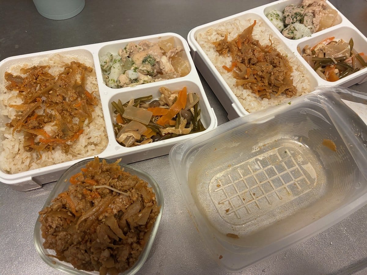 シェフの無添つくりおきのおかずを詰めた弁当2つ。ごはんの上におかずをのせ、副菜を添えている